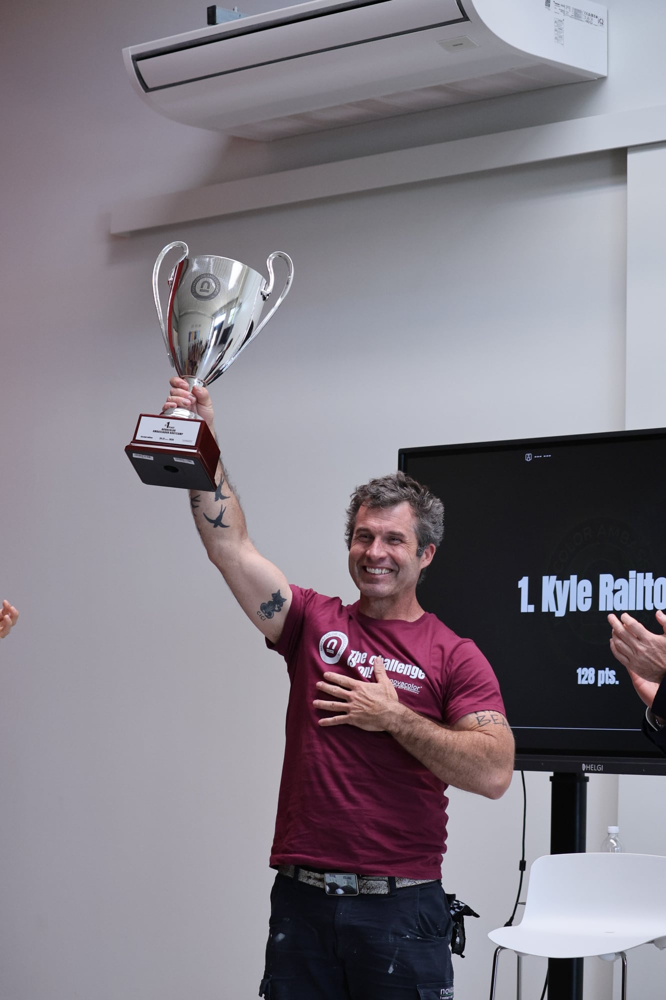 Kyle Railton holding the Novacolor Ambassador Bootcamp trophy in Venice, the screen behind him reading 1. Kyle Railton, 128 points